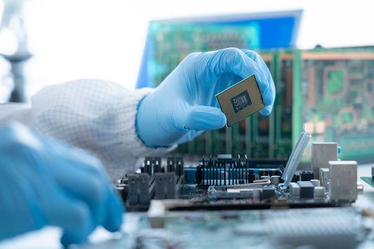 Technician wearing a blue glove holds a CPU chip over an open motherboard during assembly or repair.