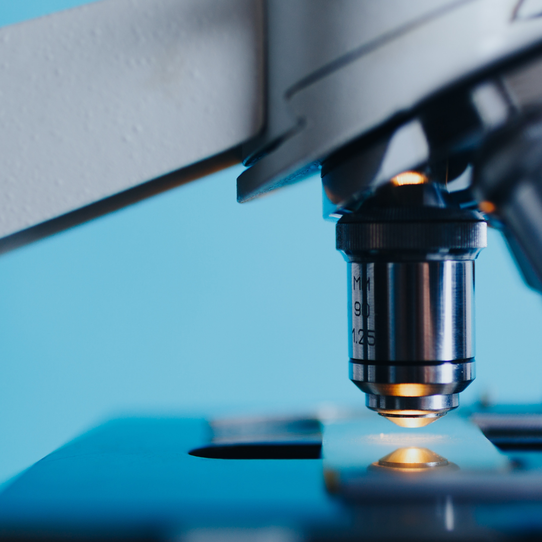 Close-up of a microscope objective lens focused on a glass slide under bright light against a blue background
